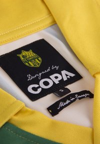Geel en groene sporttrui met een zwart label. Bevat een geborduurd FC Nantes-logo en de tekst "Ontworpen door COPA". Gemaakt in Europa.