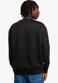 Felpa nera con scollatura rotonda, polsini e orlo a costine. Materiale in misto cotone, con una consistenza morbida e una vestibilità comoda. Design casual.