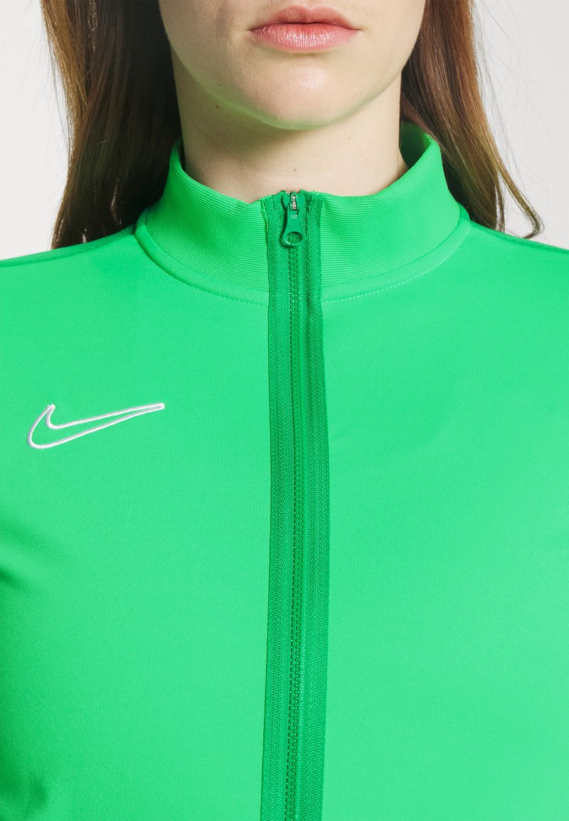 Zielona sportowa kurtka na zamek, wykonana z gładkiego, elastycznego materiału. Posiada wysoki kołnierz oraz białe logo Nike po lewej stronie klatki piersiowej.