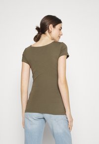 Olivengrønn tettsittende t-skjorte med korte ermer, scoop-hals og glatt bomullstoff, kombinert med lyseblå denimjeans.