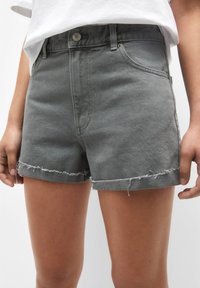 Bermudas de mezclilla gris con dobladillo deshilachado, cinco bolsillos y cierre de botón en la parte delantera. El material parece suave con una textura sutil.
