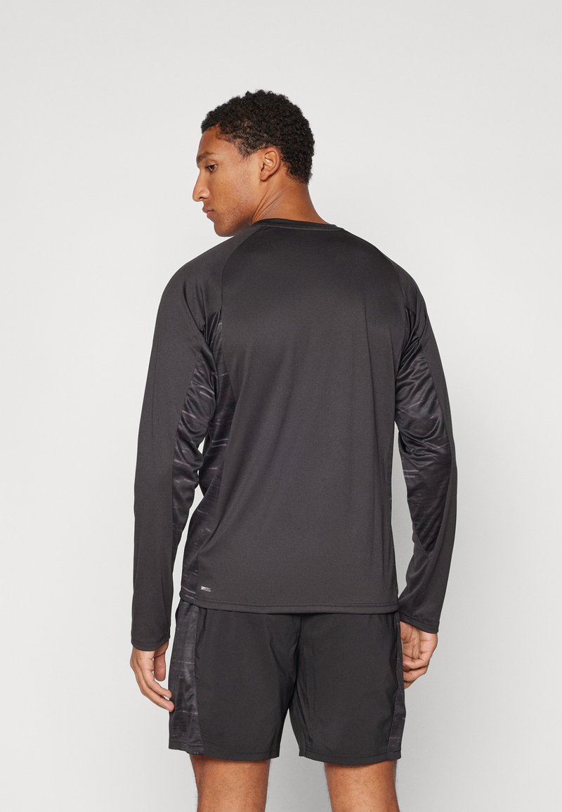 Czarna sportowa koszulka z długim rękawem z kontrastującymi, teksturowanymi rękawami, z okrągłym dekoltem i lekkiego materiału. W połączeniu z czarnymi szortami.