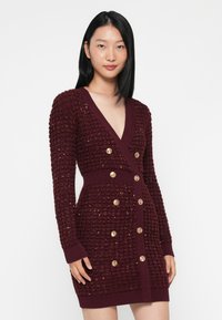 Abito lavorato a maglia bordeaux con scollo a V, maniche lunghe, tessuto testurizzato e dettagli in ottone lungo il davanti e in vita.