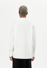 White shirt with a pointed collar, long sleeves, and a relaxed fit. Smooth fabric, paired with a black pleated skirt. Minimalist design.