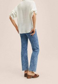 Blusa blanca texturizada, corte relajado; jeans acampanados de estampado paisley en azul; sandalias de tacón cuadrado marrones con tachuelas doradas.