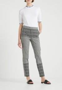 T-shirt blanc avec bord noir, associé à un pantalon à carreaux gris avec poches latérales et sandales noires plates. Coupe ajustée, tissu lisse.