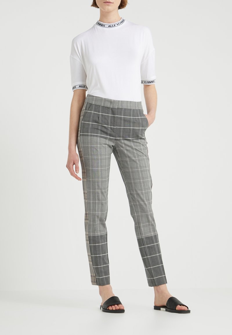 T-shirt blanc avec bord noir, associé à un pantalon à carreaux gris avec poches latérales et sandales noires plates. Coupe ajustée, tissu lisse.