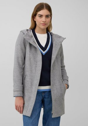 Manteau en mélange de laine gris avec capuche, doté d'une fermeture éclair, de poches latérales et de poignets côtelés. Porté par-dessus un pull rayé bleu marine et bleu clair.