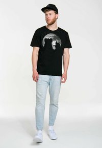 Černé bavlněné tričko s šedou grafikou Cookie Monstra s velkými očima a sušenkou, v kombinaci s světle modrými džíny a bílými teniskami.