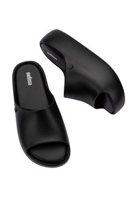 Sandales à glissière en caoutchouc noir avec un design ouvert à l'avant et sans dos. Texture lisse, style minimaliste et logo de la marque en relief sur la semelle intérieure.