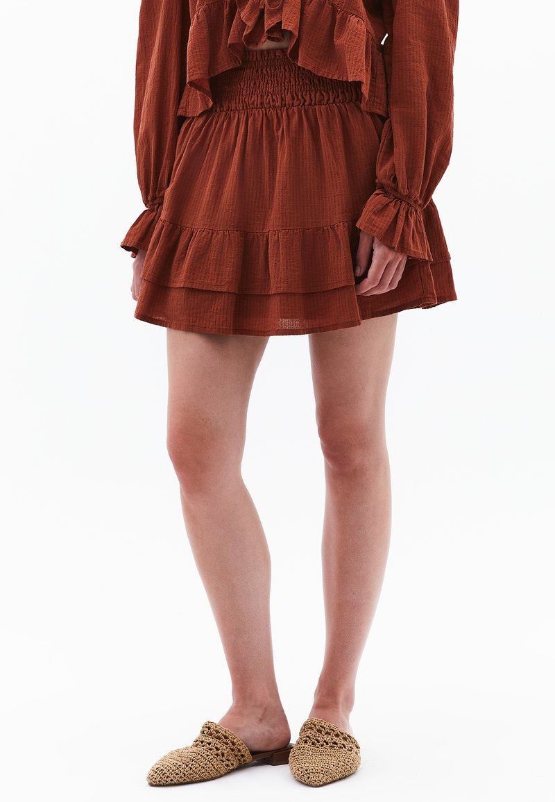 Roodbruine tiered jurk met een smocked taille en ruches mouwen, gemaakt van lichte stof. Gecombineerd met geweven instap schoenen.