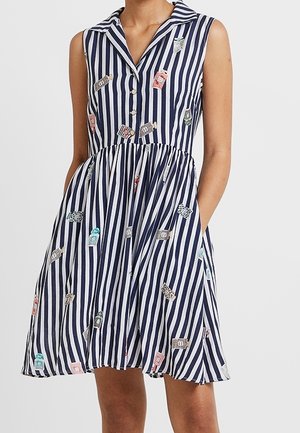Bezrękawowa sukienka w pionowe paski w kolorze granatowym i białym z kołnierzykiem, guzikami, kieszeniami oraz rozrzuconymi kolorowymi nadrukami butelek perfum.