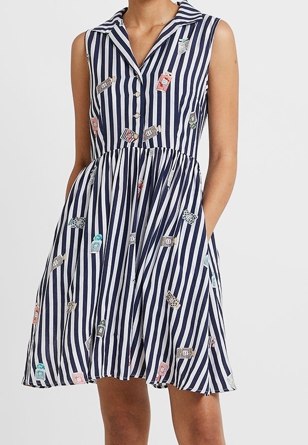 Robe sans manches à rayures verticales bleu marine et blanches avec col, boutons, poches et imprimés dispersés de bouteilles de parfum colorées.