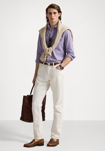 Cămașă button-up de culoare mov deschis, pulover crem așezat pe gât, pantaloni albi, pantofi din piele maro și geantă de umăr maro închis.