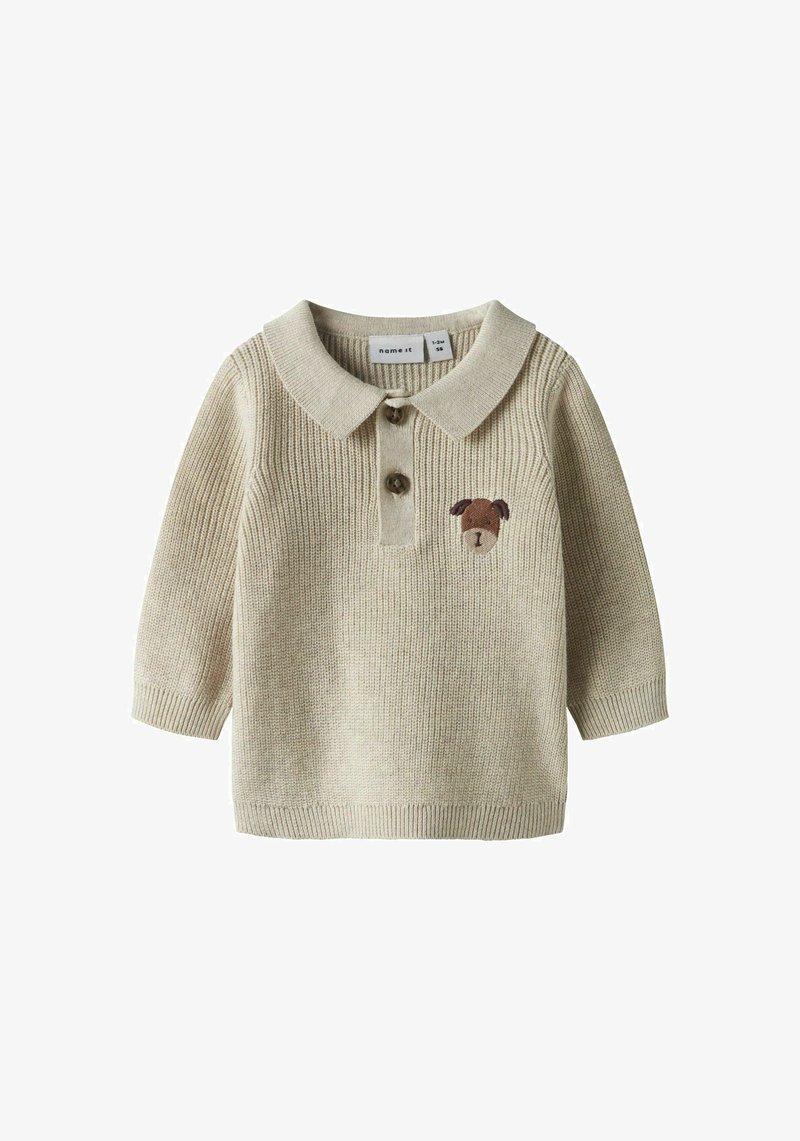 Polo beige a maglia con maniche lunghe, caratterizzata da una patta con due bottoni e un ricamo marrone a forma di cane sul petto. Materiale morbido e dalla texture.