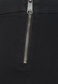 Černé kalhoty se zipem s metalickým zipem a hladkým textilním povrchem, s čistým, moderním designem. Doplňky zahrnují označený zip.