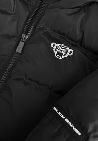 Zwarte pufferjack met een glanzende, gladde textuur. Heeft een opvallend wit geborduurd logo en een ritssluiting aan de voorkant. Bevat een label met de tekst "BLCK BNNS."
