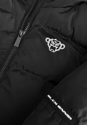 Zwarte pufferjack met een glanzende, gladde textuur. Heeft een opvallend wit geborduurd logo en een ritssluiting aan de voorkant. Bevat een label met de tekst "BLCK BNNS."