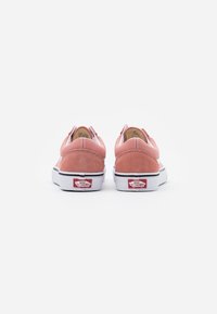 Baskets de skate en suède rose avec semelles blanches, présentant un profil bas, un embout rond, des accents élastiques sur les côtés et le branding classique de Vans sur le talon.