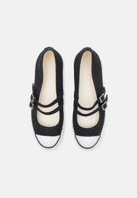 Zapatillas de lona negra con dos correas de hebilla, punta redonda y acentos de goma blanca. Plantilla texturizada con un patrón de diamante.