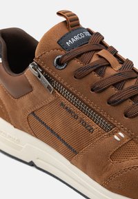 Brune semsket og mesh sneakers med glidelåsdetalj, mørke snørebånd og MARCO TOZZI merkevare. Hvit såle med teksturerte detaljer.