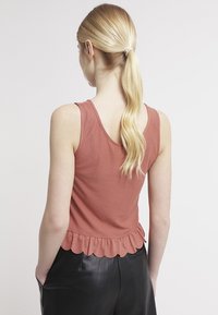 Top sin mangas de color rosa polvo con dobladillo en forma de scallop, hecho de una tela suave. Presenta un diseño holgado.