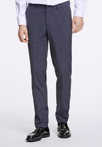 Marinblå randiga byxor i strukturerad textil, med flat front, bälteöglor och skräddarsydd passform, kombinerade med svarta finskor.