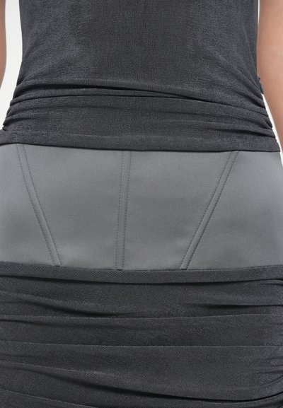 Fekete réteges ruhadarab, melynek felső része texturált, redőzött, az alsó része sima szürke panel, kiemelve varrási részletekkel.