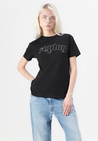 Fekete pamut póló rövid ujjakkal és kerek nyakkal, a mellkason fehér "replay" felirattal, stilizált betűtípussal.