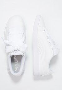 Sneakers atletici bianchi con una parte superiore in sintetico liscio, suola in gomma testurizzata e lacci a nastro. Dettaglio del logo discreto sulla soletta.