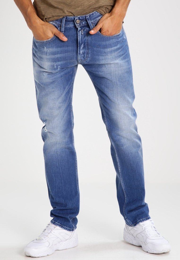 Jeans de mezclilla azul con un acabado desvaído, ligero desgaste, diseño de cinco bolsillos y corte recto. Llevados con zapatillas blancas.