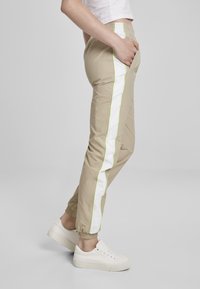 Beige joggebukser med elastisk liv, sidelommer, hvite og neongrønne sidestriper, smale mansjetter; paret med hvite sneakers.