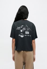 Schwarzes Baumwoll-T-Shirt mit kurzen Ärmeln, das auf der Rückseite eine weiße Linienzeichnung verschiedener Trinkgefäße und den Schriftzug "TAKE YOUR TIME" zeigt.