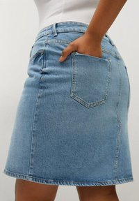 Jupe en denim bleu clair avec une taille ajustée et une silhouette évasée. Présente une poche arrière et des détails de couture subtils le long de l'ourlet.