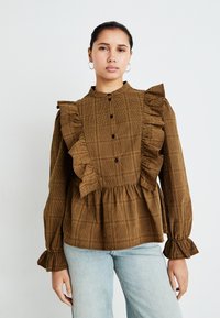 Blusa a quadri marrone con accenti arricciati, maniche lunghe, collo alto e chiusura con bottoni davanti; realizzata in tessuto testurizzato.