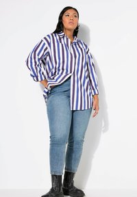 Camisa de gran tamaño a rayas en púrpura y blanco, con diseño de botones, mangas largas, combinada con jeans ajustados azules y botas negras por encima del tobillo.