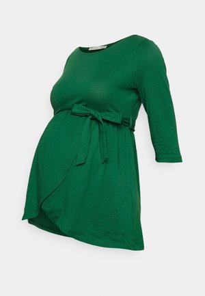 Haut de maternité vert à manches 3/4 avec ceinture assortie en tissu à nouer au-dessus de la taille, fabriqué en matériau doux et extensible.