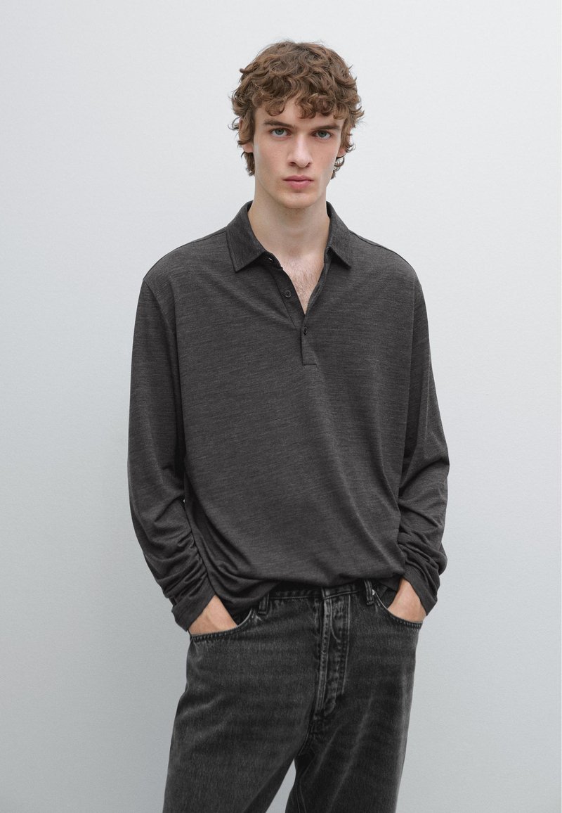 Mørkegrå långærmet polo med knaplukning ved kraven, lavet af blødt stof, kombineret med mørke jeans. Modellen står med hænderne i lommerne.