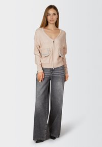 Rosa gestrickte Strickjacke mit Reißverschluss, ausgestattet mit zwei verzierten Taschen und gerippten Bündchen, kombiniert mit grauen, weit geschnittenen Jeans.