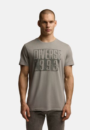 Szara koszulka z krótkim rękawem z dużym graficznym nadrukiem z napisem "DIVERSE 1993" w ciemnoszarym kolorze. Prosty, okrągły dekolt, wykonana z teksturowanej tkaniny.