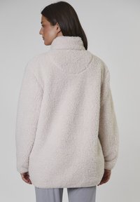 Ljusröd fleece-tröja med hög krage, överdimensionerad passform och texturerad yta. Har långa ärmar och en böjd fåll.