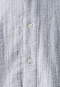 Tejido a rayas azul claro con dos botones blancos alineados verticalmente en la tapeta de una camisa.