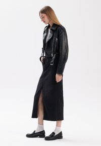 Zwarte leren motorjack met zilveren ritsen, gecombineerd met een zwart denimrok met hoge taille en een voorsplit. Zwarte loafers en grijze sokken.