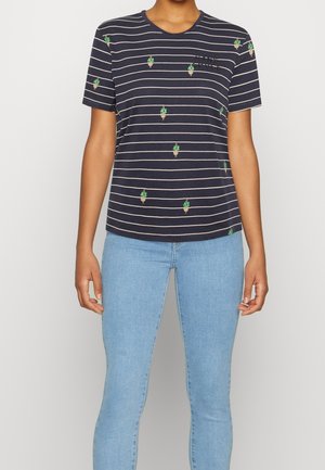 Marineblaue T-Shirt mit dünnen weißen horizontalen Streifen und kleinen grünen Kaktusmustern, getragen zu hellblauen Jeans.