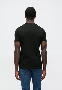 Μαύρο βαμβακερό t-shirt με κοντά μανίκια. Διαθέτει στρογγυλή λαιμόκοψη και ομαλή υφή, φορεμένο με μπλε τζιν παντελόνι.