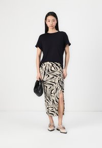 Zwart t-shirt met korte mouwen, gecombineerd met een beige en zwart gestreepte midi-rok met een zijsplit, terwijl er een zwarte tas wordt vastgehouden.