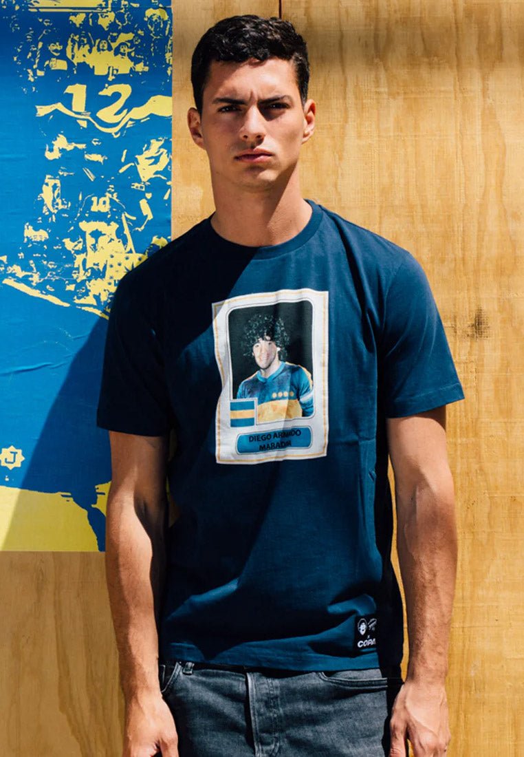 Navyblauwe katoenen t-shirt met een grafische print van een speler in een omrand ontwerp. Draag het met grijze jeans tegen een houten achtergrond.