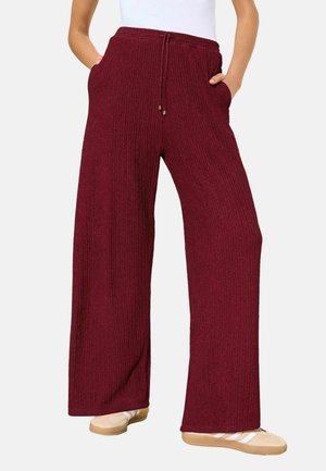 Bordeauxrote, gerippte Weite-Hosen mit Kordelzug in der Taille, seitlichen Taschen und einer strukturierten Oberfläche, kombiniert mit weichen, beigen Schuhen.
