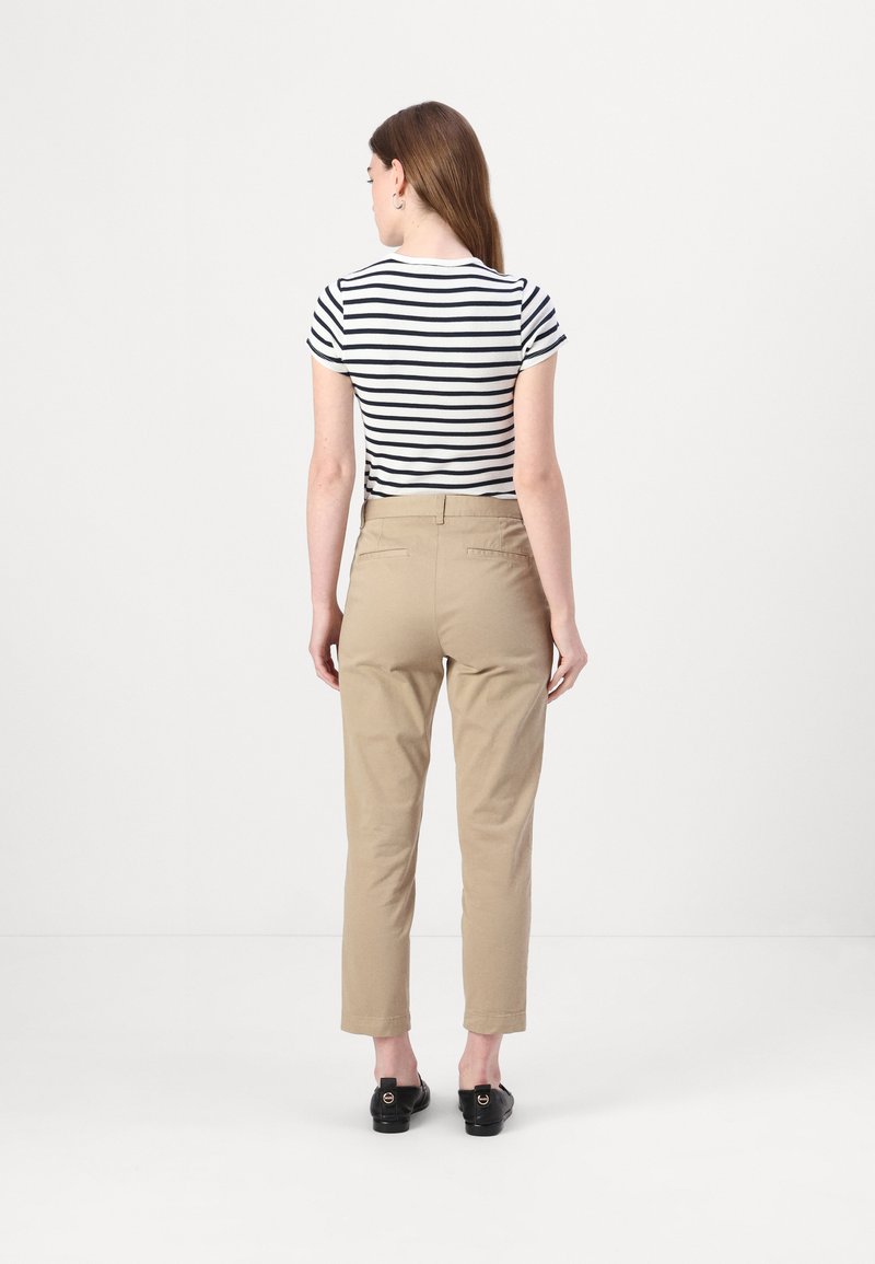 Beige Hosen mit maßgeschneiderter Passform und Gesäßtaschen, kombiniert mit einem kurzärmeligen Oberteil in Schwarz und Weiß mit Streifen. Auf einem einfarbigen Hintergrund.