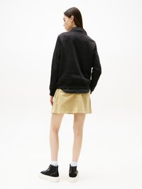 Svart hettegenser med tekstur, stylet med en khaki miniskjørt. Båret med svarte høye sneakers og hvite ankelstrømper.